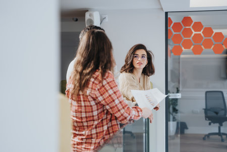 Confident businesswoman holding documents chatting with colleague in modern office.の写真素材