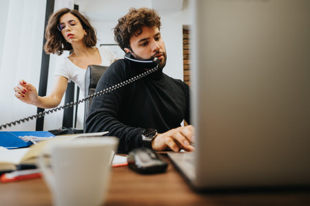 Busy male professional multitasking with phone and computer at desk with female colleague.の写真素材