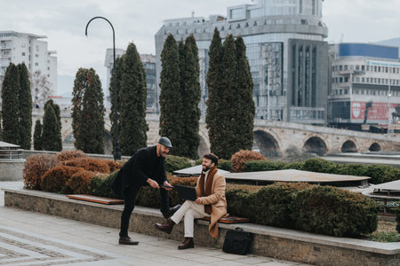 Two businessmen engage in a serious discussion over a laptop while sitting outside. They are focused, exchanging ideas, and working collaboratively.の写真素材