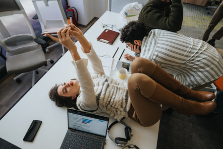 Brunette woman lying on a working desk, taking a selfie while resting from work.の写真素材