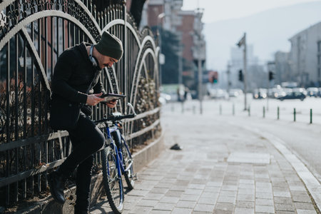 Young man in a beanie using smart phone with headphones by a bike in the city