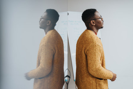 A thoughtful African American man stands in an office, representing concepts like reflection, planning, and strategy in a professional environment.の写真素材