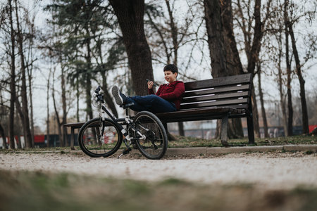 Young boy resting on a park bench with his bicycle enjoying the outdoors