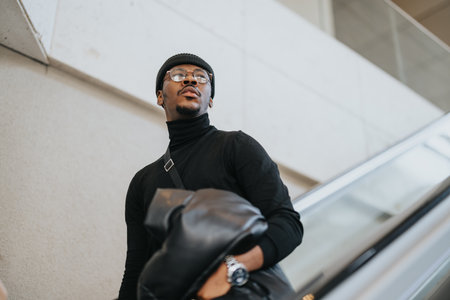Confident young black businessman in casual attire with stylish eye wear and leather bag.の写真素材