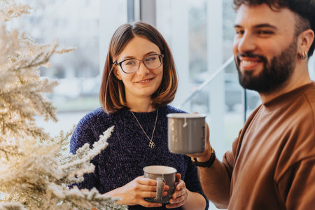 Two cheerful friends enjoying a warm conversation over coffee next to a festive Christmas tree, radiating friendship and holiday spirit.の写真素材