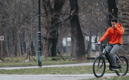 Young man in a red hoodie riding a bicycle in the park on a cloudy dayの写真素材