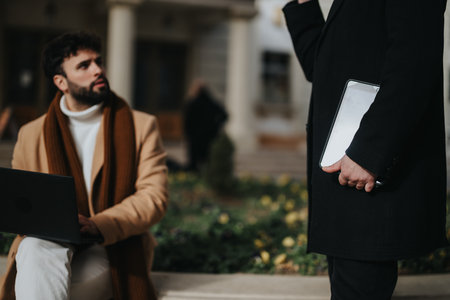 Two professional men engaging in a discussion outdoors with technologyの写真素材