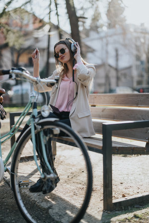 Stylish young woman enjoying music on headphones in a city park with her bicycleの写真素材