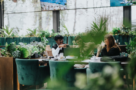 Multiracial business colleagues working together in a casual cafe setting, with laptops and coffee,...