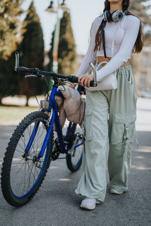 Stylish young woman with headphones standing with bicycle in the city.