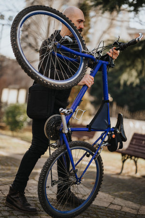 Active young adult carrying a blue mountain bike in an urban park setting