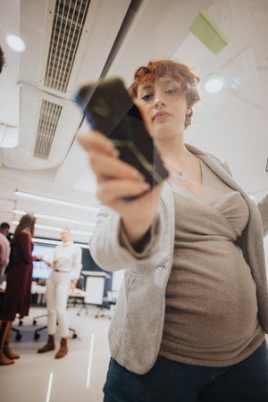 Redhead, pregnant woman writing statistics or new strategy on a glass wall at modern workspace.の写真素材