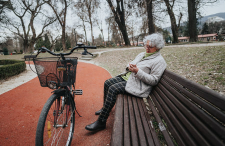 Active senior woman enjoying a break on park bench with bicycleの写真素材