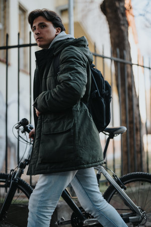 Young man in winter coat with backpack mounts bicycle on city streetの写真素材