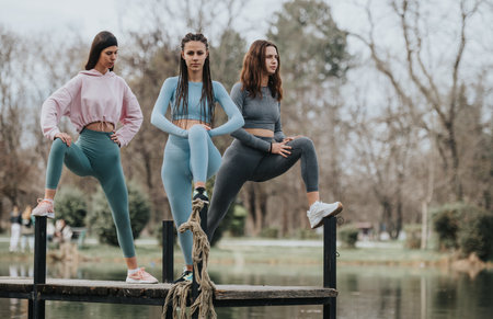 Three women in sportswear stretching on a wooden jetty in a park settingの写真素材