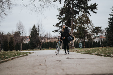 Active woman walking with bicycle in urban park during autumn season.