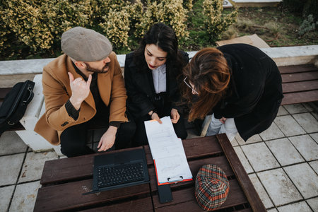 Overhead view of three businesspeople having a meeting outdoors with documents and laptop on a wooden table.の写真素材