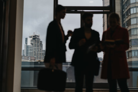 Silhouetted professionals discussing work in a modern office with cityscape backgroundの写真素材