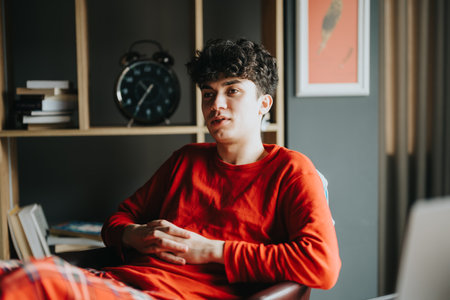 Young man in red sweater looking pensive at home.
