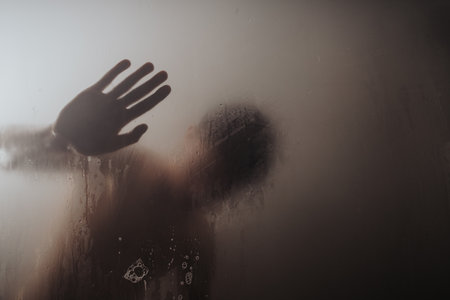 Silhouette of a person behind a steamy glass with hand print