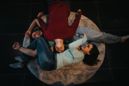 Joyful friends laying on floor rug, laughing and having fun together.