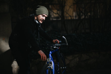 Urban cyclist with headphones standing outdoors beside a blue bicycleの写真素材
