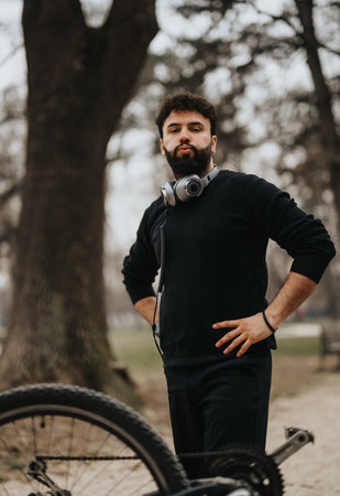 Confident businessman in casual attire taking a break with his bicycle in a park.の写真素材