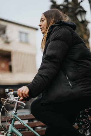 Side profile of a determined young female cyclist in a warm coat enjoying a bike ride in the city on...