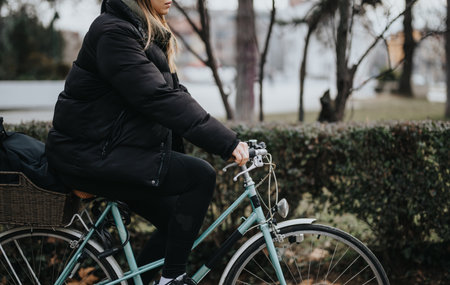 Side view of a young female cyclist dressed in warm winter clothing taking a break during a bicycle...