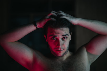 Man in contemplation with hands behind head against dark background.