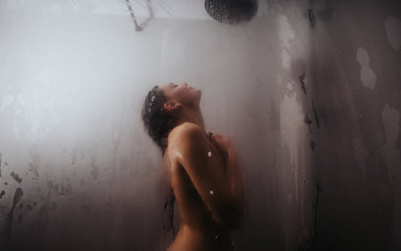 Young woman enjoying a relaxing shower with steam and water droplets aroundの写真素材