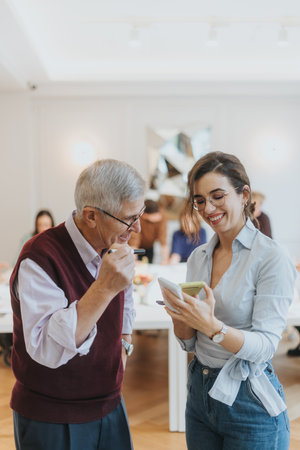 Senior man laughing with young woman holding smart phone in casual office