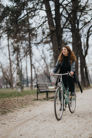 Stylish young businesswoman riding a bicycle in a park, embodying elegance and confidenceの写真素材