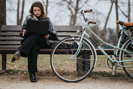 Young businesswoman working on laptop in park with bicycleの写真素材