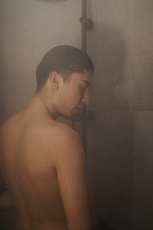 Serene young adult enjoying a hot shower in a modern bathroom