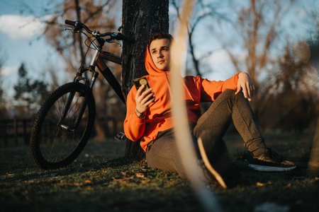 Young man relaxing with his bike in the park at sunsetの写真素材