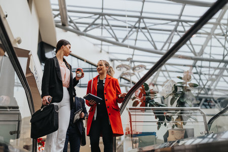 Businesswomen walking on escalator in modern buildingの写真素材