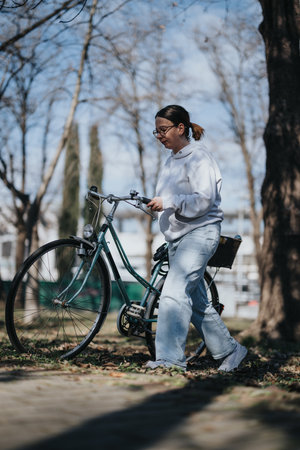 A young adult woman enjoying a sunny day in the park with her vintage bicycle. Casual lifestyle and eco-friendly transport concept.の写真素材