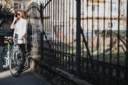 Stylish woman talking on phone while leaning on a bicycle in the cityの写真素材