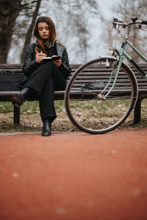 Elegant young businesswoman writing notes while sitting on a park benchの写真素材