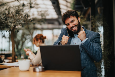 Enthusiastic businessman celebrating success with laptop at cafeの写真素材