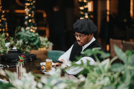 A stylish young businessman is fully concentrated on his smart phone at a modern coffee shop adorned...