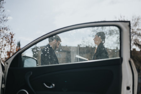 Two people conversing beside a car on a sunny dayの写真素材