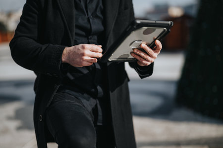 Stylish businessman using tablet for work outdoors on sunny day.