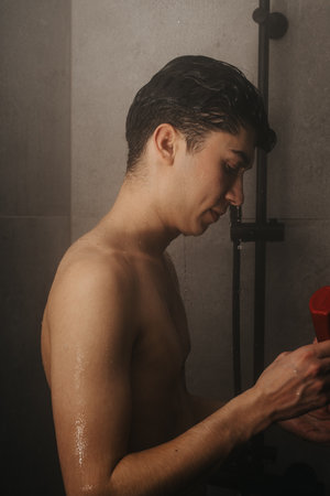 Young man taking a shower, washing hair with shampoo in modern bathroomの写真素材