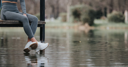 Athletic woman in fitness gear resting by tranquil lakeの写真素材