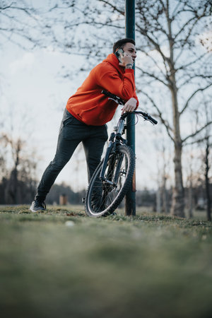 Young man with bicycle in park talking on phone, leisure time outdoorsの写真素材