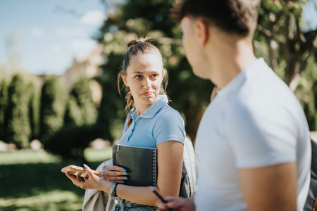 Young students engage in a discussion while studying in a sunny urban parkの写真素材