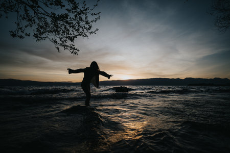 Joyful girl experiencing freedom at the lake during a beautiful sunsetの写真素材
