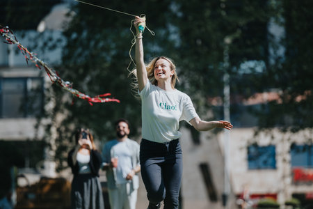 Joyful woman flying a kite in the park with friends enjoying a sunny dayの写真素材